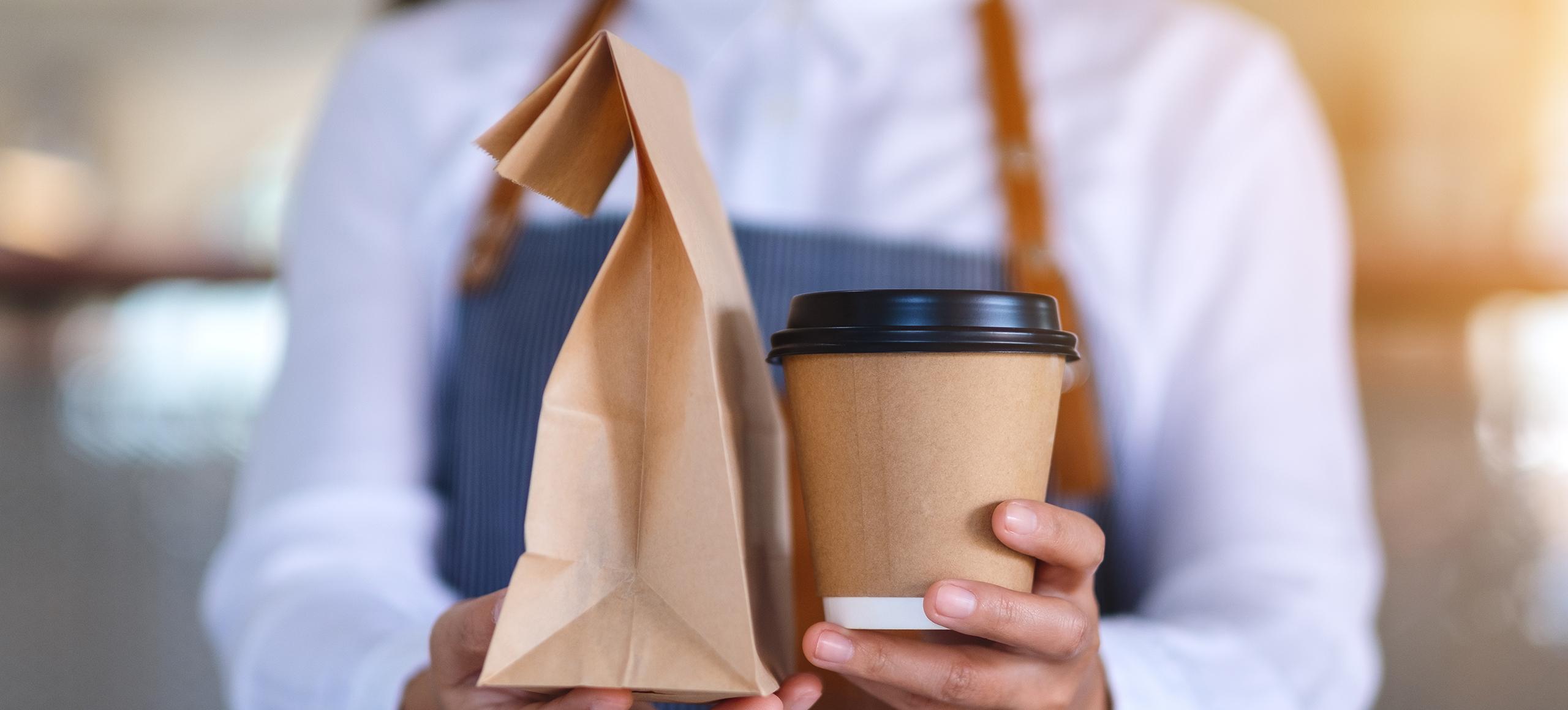 A person holding a takeaway bag and cup.
