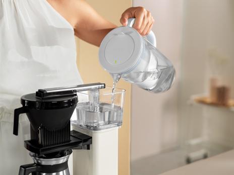 Woman pours water from glass jug into coffee machine