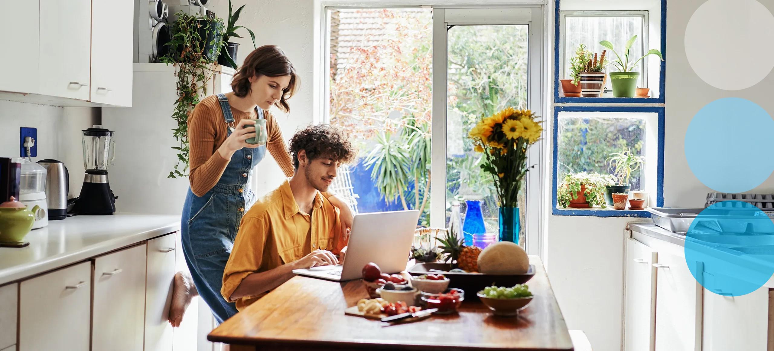 Young couple in kitchen looking at laptop.
